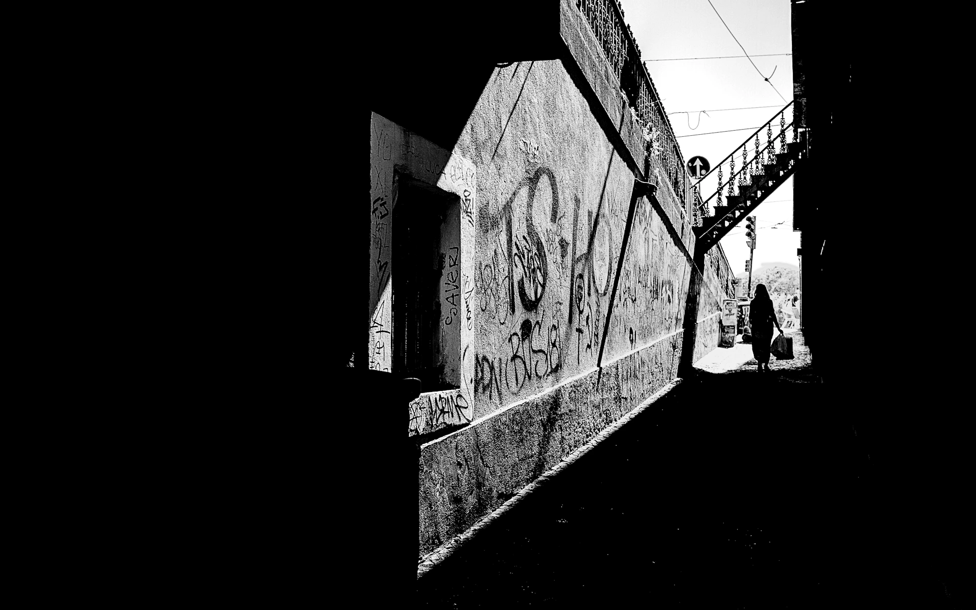 A striking black and white street scene captured with a Ricoh GR, showing a lone figure walking past textured urban walls.