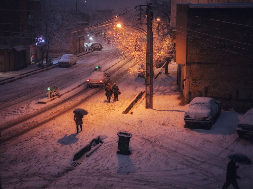 três pessoas caminhando na calçada ao lado de estrada coberta de neve