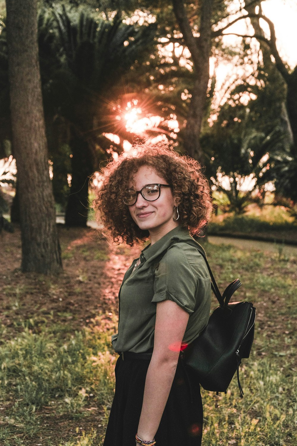 femme souriante portant un haut gris debout près d’arbres verts