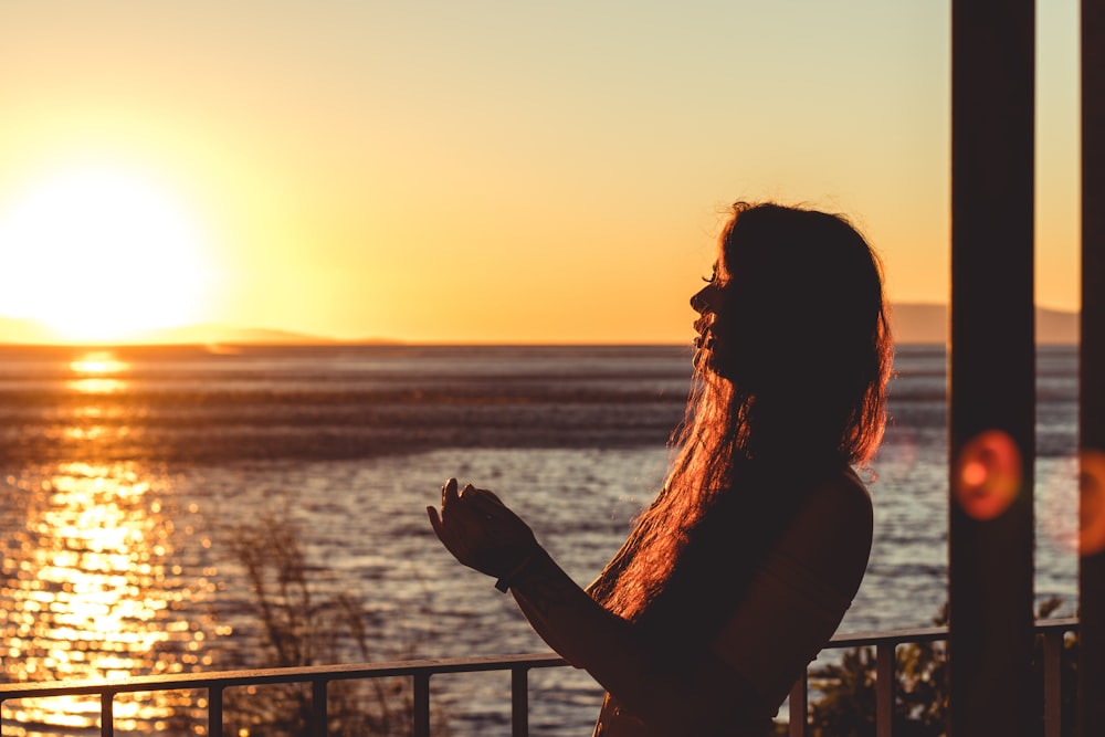 silhouette de femme à côté des balustrades devant le soleil