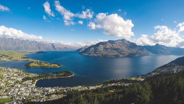 buildings near body of water and mountains under clear blue sky and white clouds at daytime