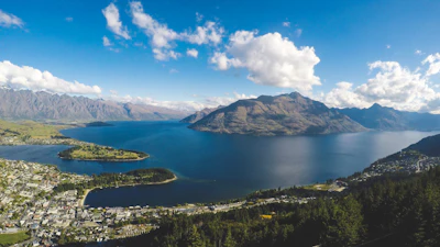 buildings near body of water and mountains under clear blue sky and white clouds at daytime