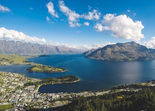 buildings near body of water and mountains under clear blue sky and white clouds at daytime