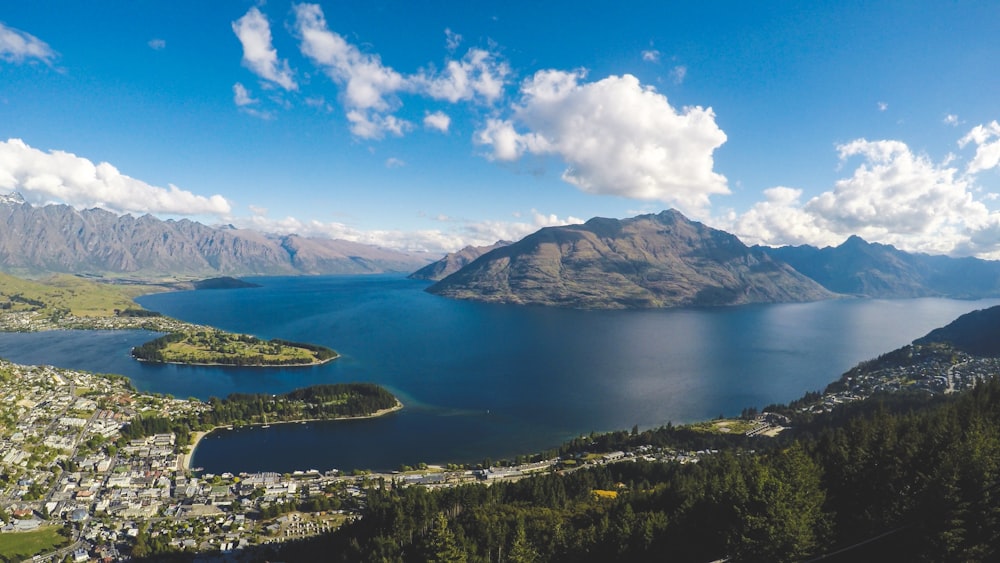 buildings near body of water and mountains under clear blue sky and white clouds at daytime