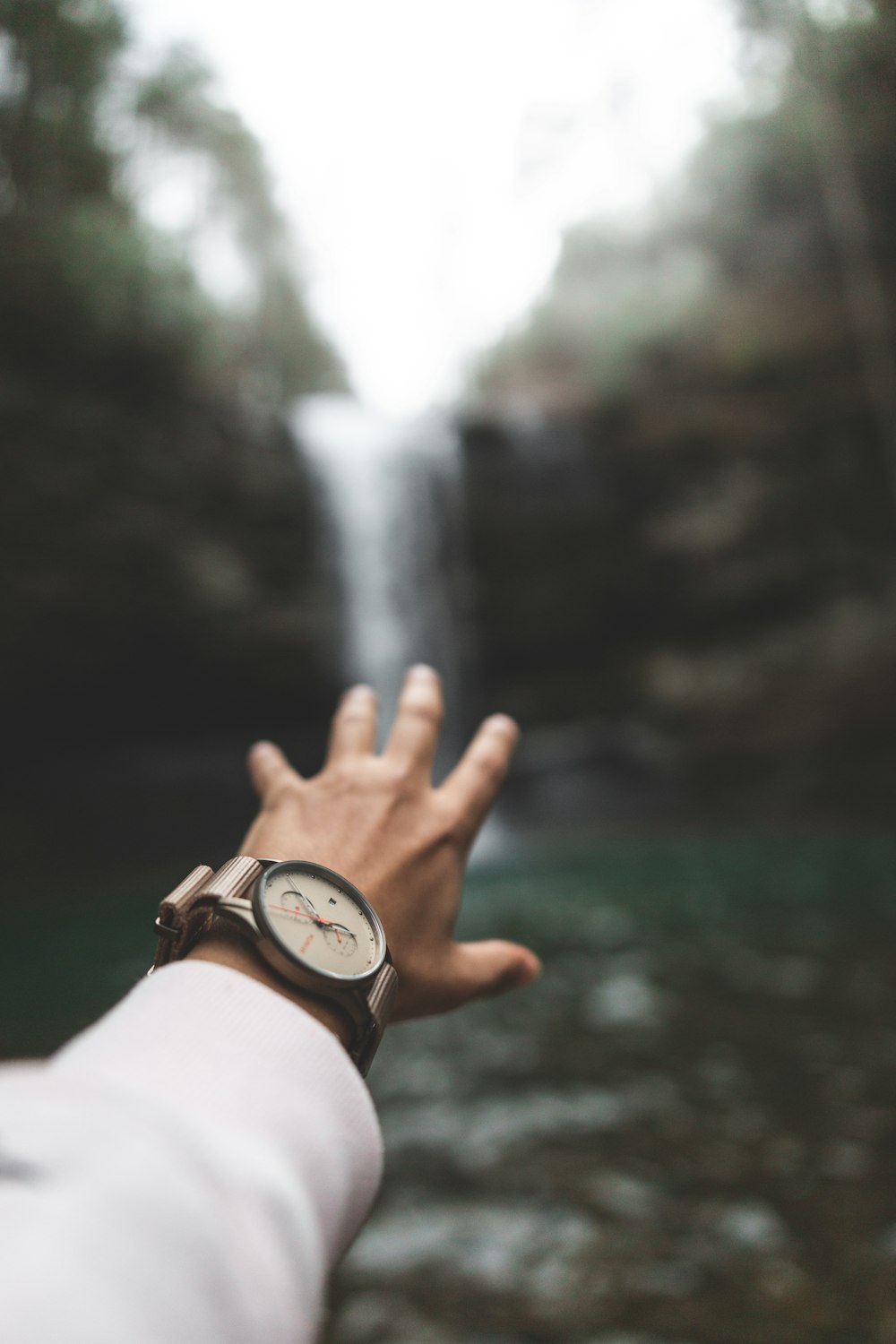 selective focus photography of man reaching out to waterfalls