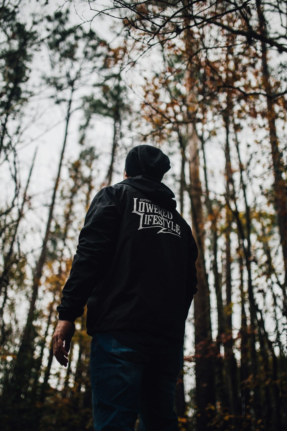 man wearing black hoodie and blue jeans standing in front of trees