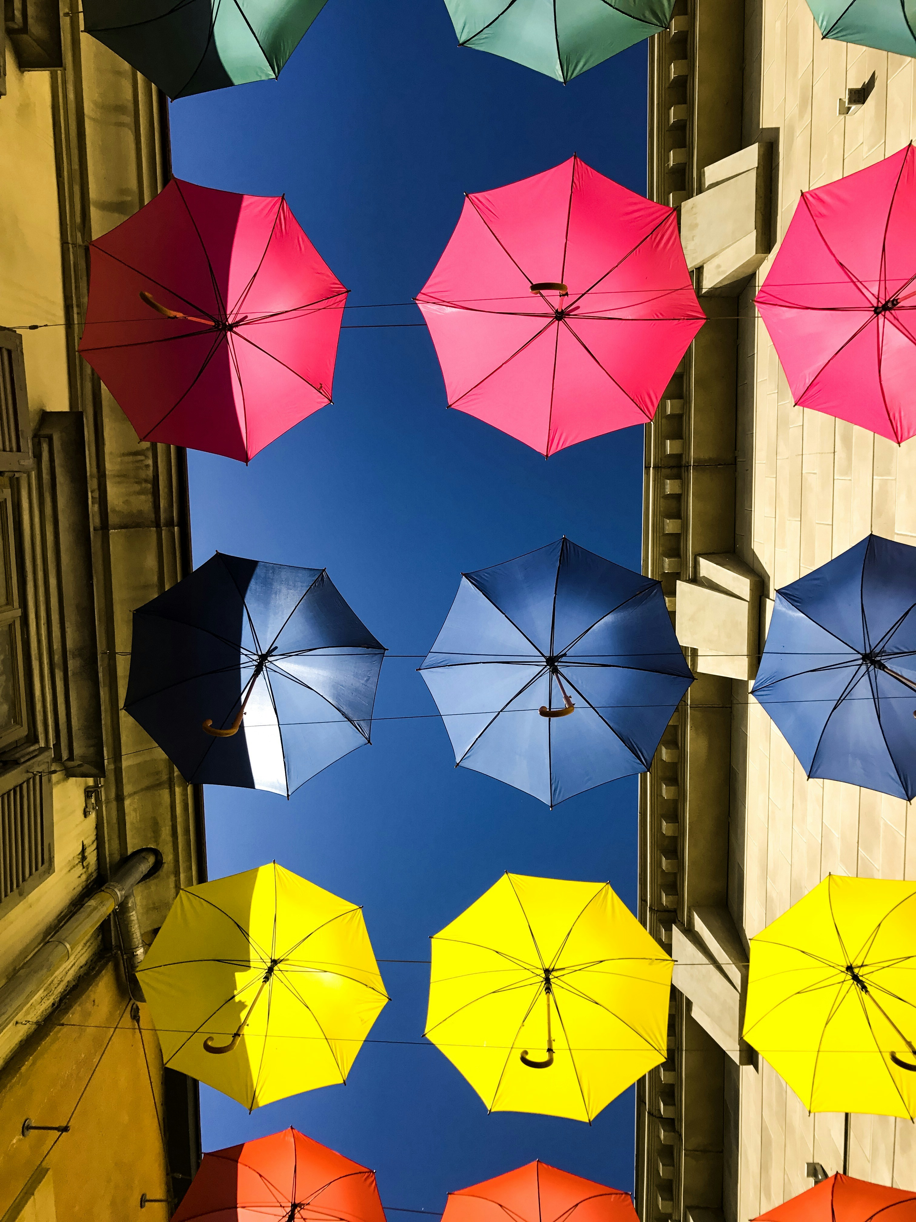 green, pink, blue, yellow, and orange umbrellas hanging in between buildings