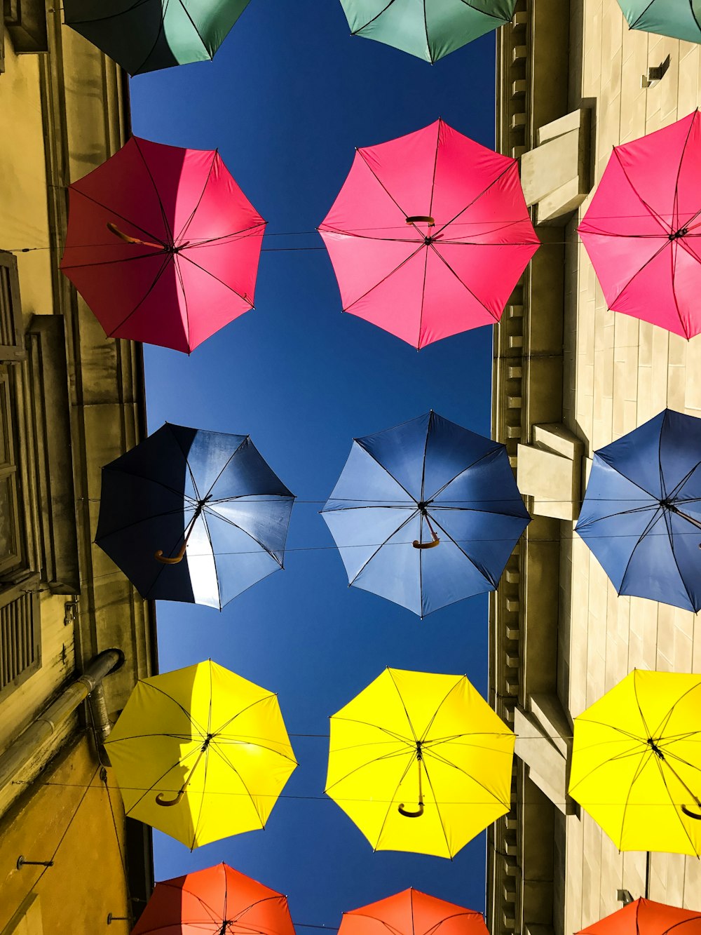 green, pink, blue, yellow, and orange umbrellas hanging in between buildings