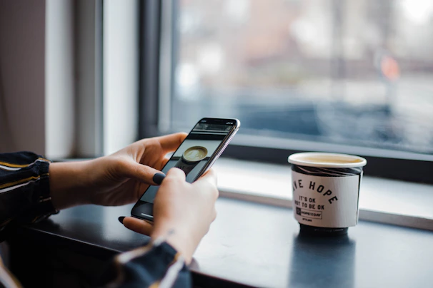 A smiling young woman reading an inspirational article on her smartphone while sitting in a cozy café.