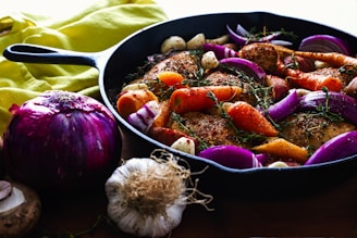carrots, garlic, onions, and herb spicing meat on skillet