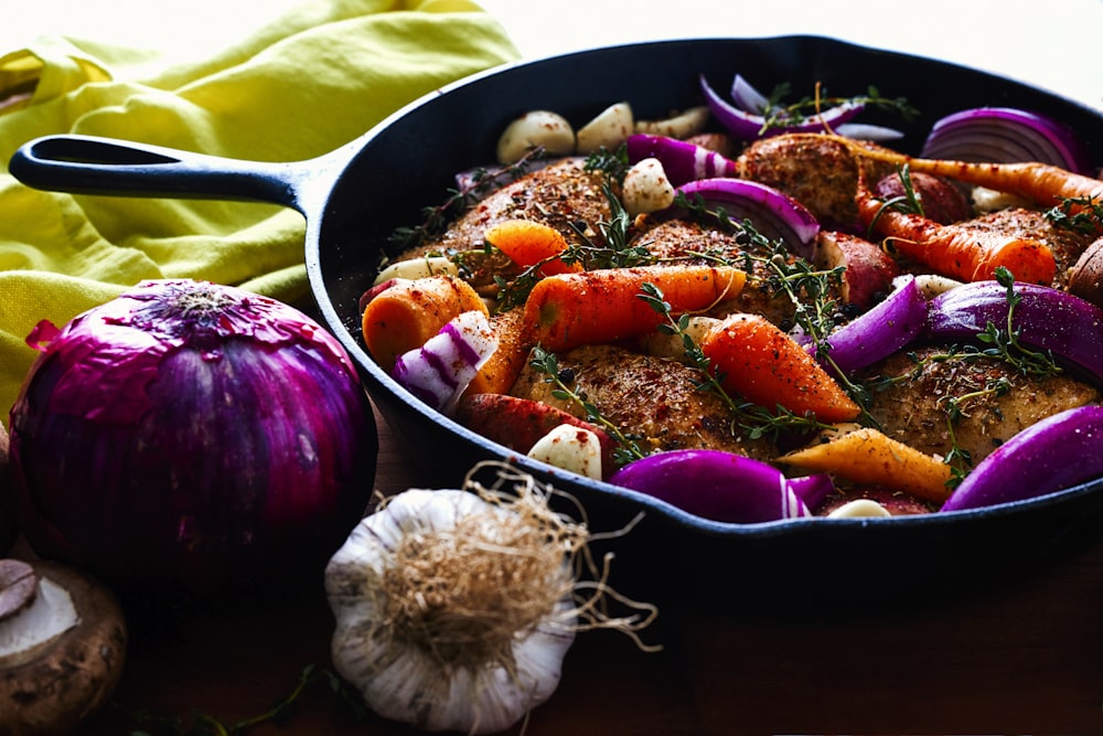 carrots, garlic, onions, and herb spicing meat on skillet