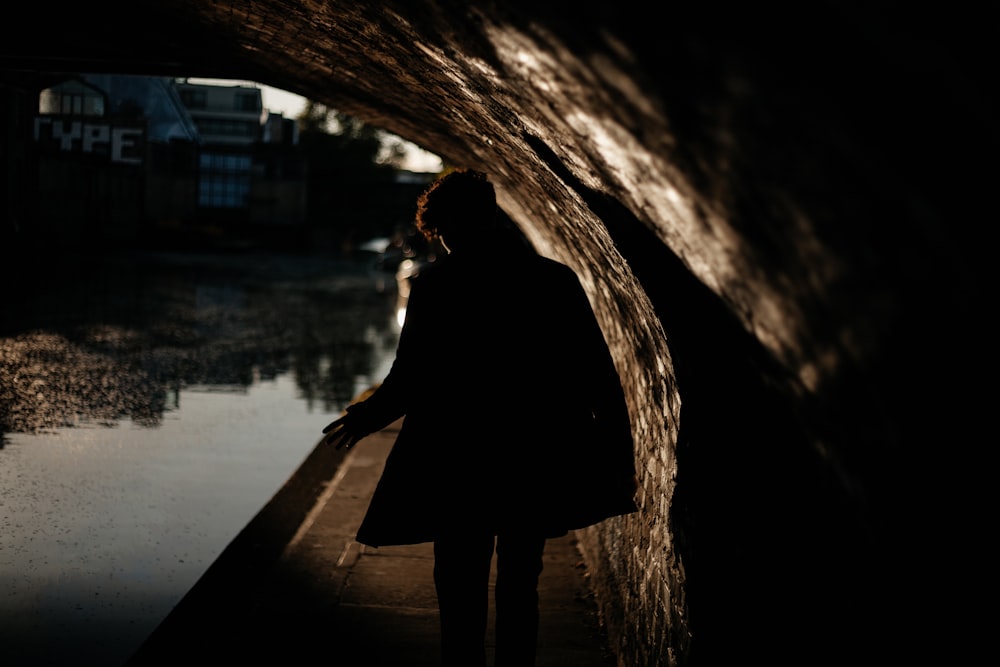 person wearing black coat walking under the bridge