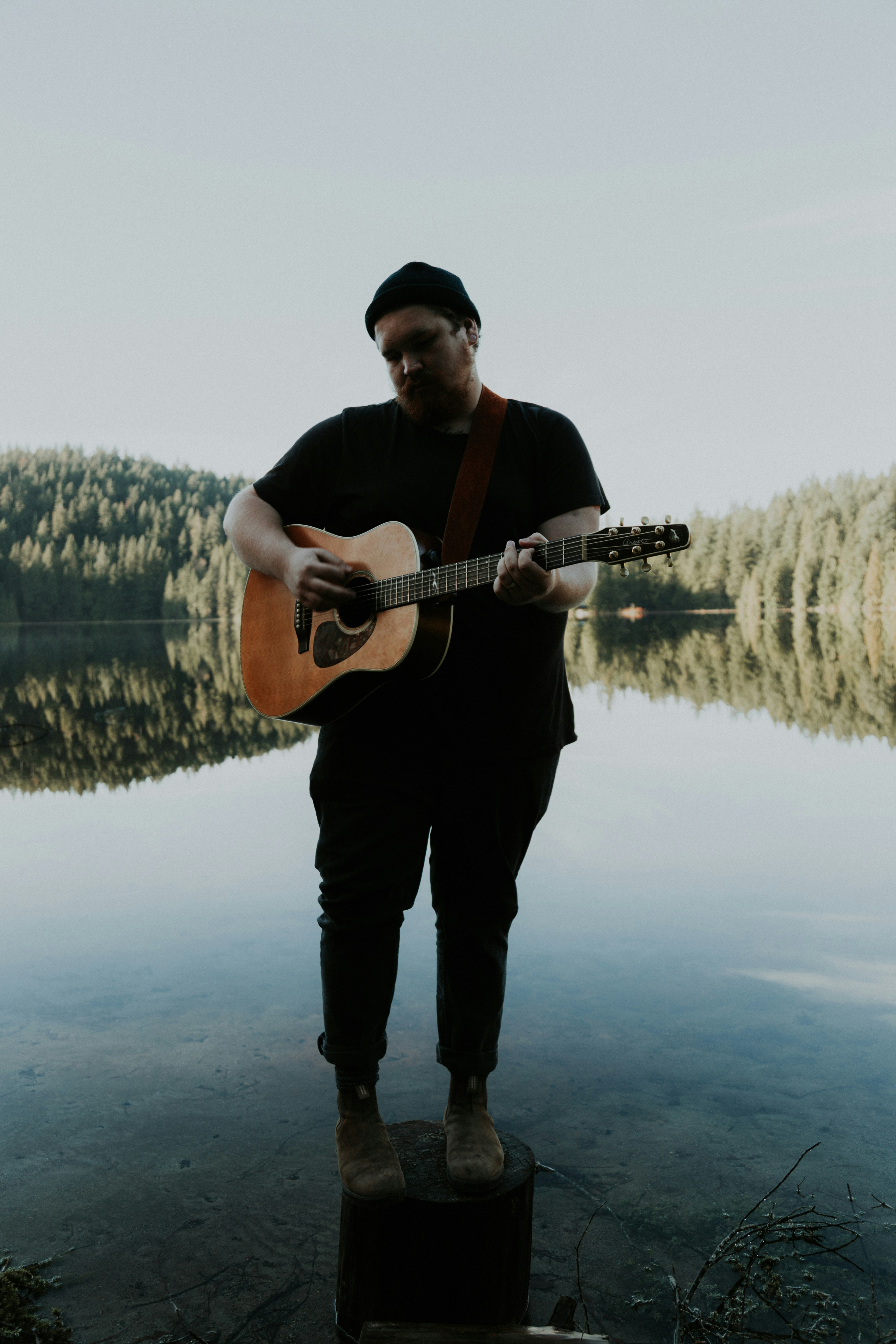 man standing on wooden post playing guitar