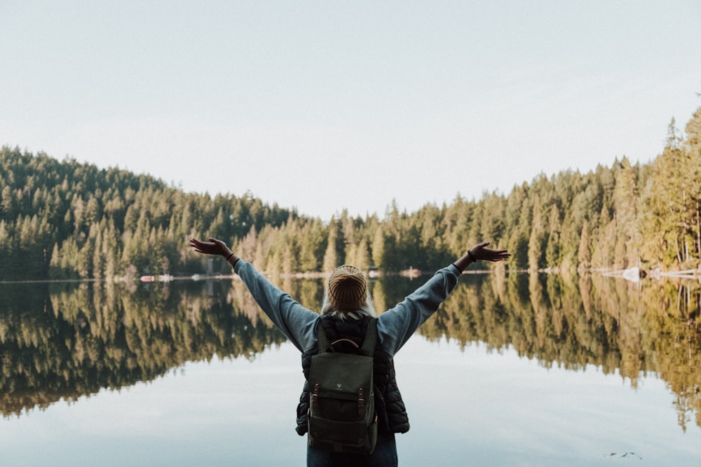 woman open her arms facing calm body of water