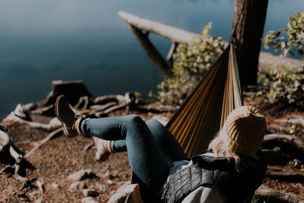 woman sitting on hammock beside calm water