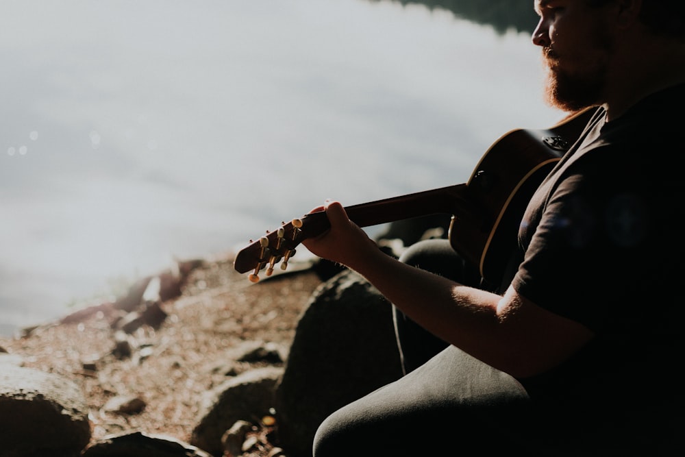 man sitting on shore while playing guitar