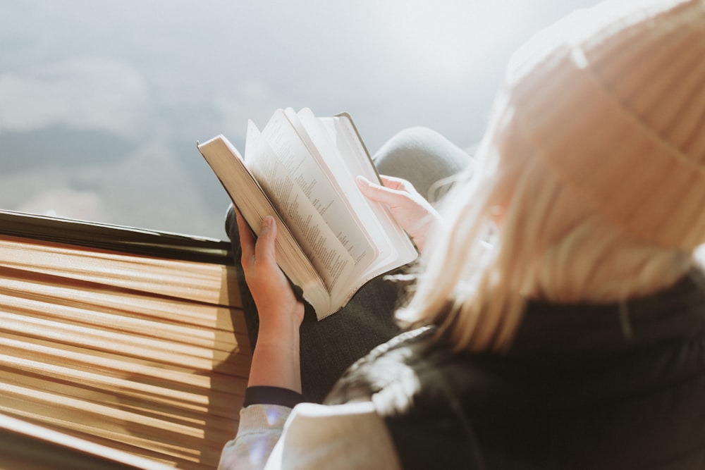 woman sitting on brown ledge while holding book