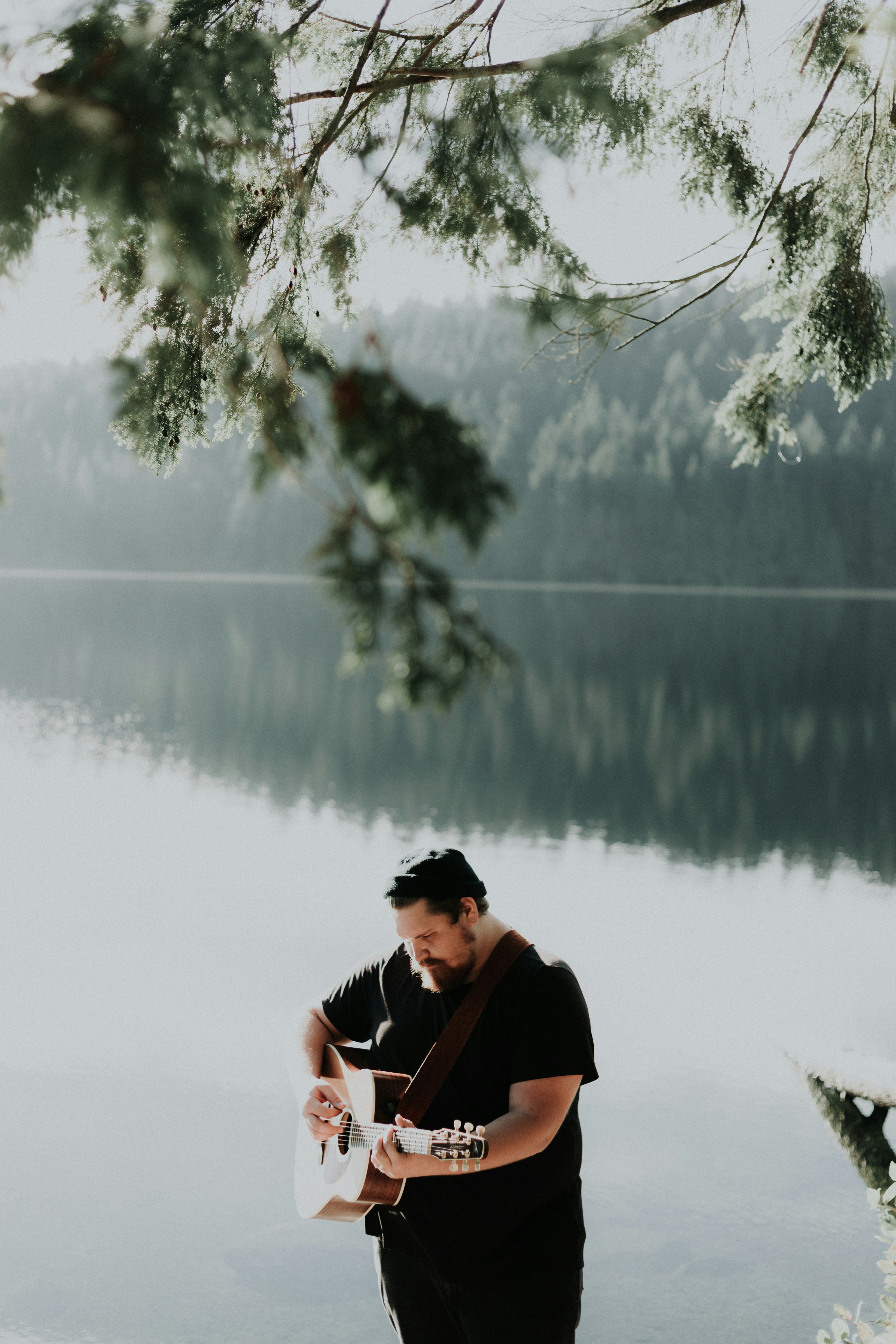 man playing brown acoustic guitar near body of water