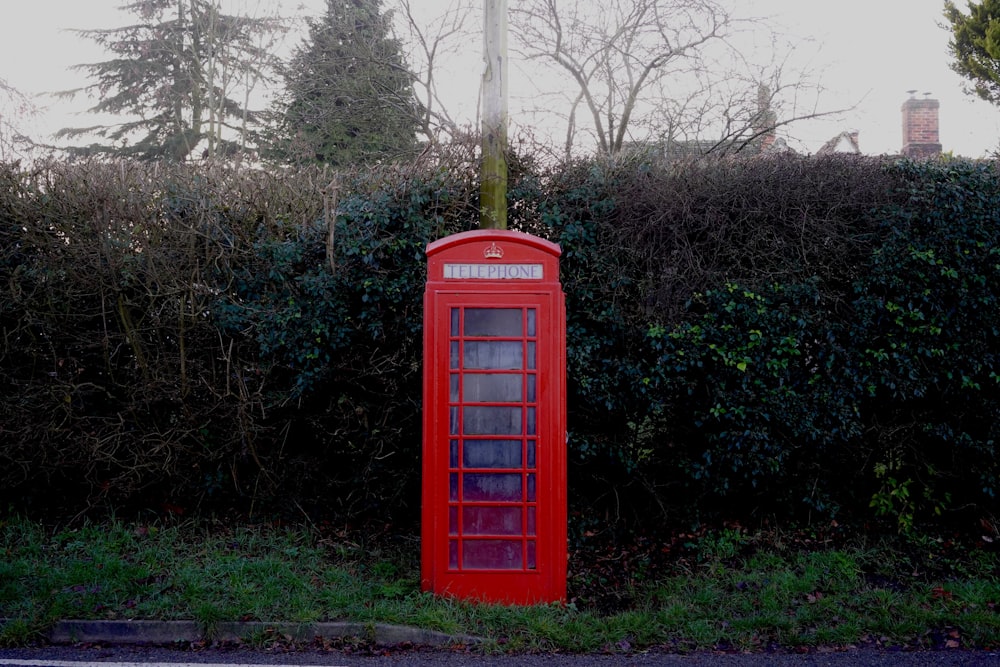 cabine téléphonique rouge devant la topiaire verte