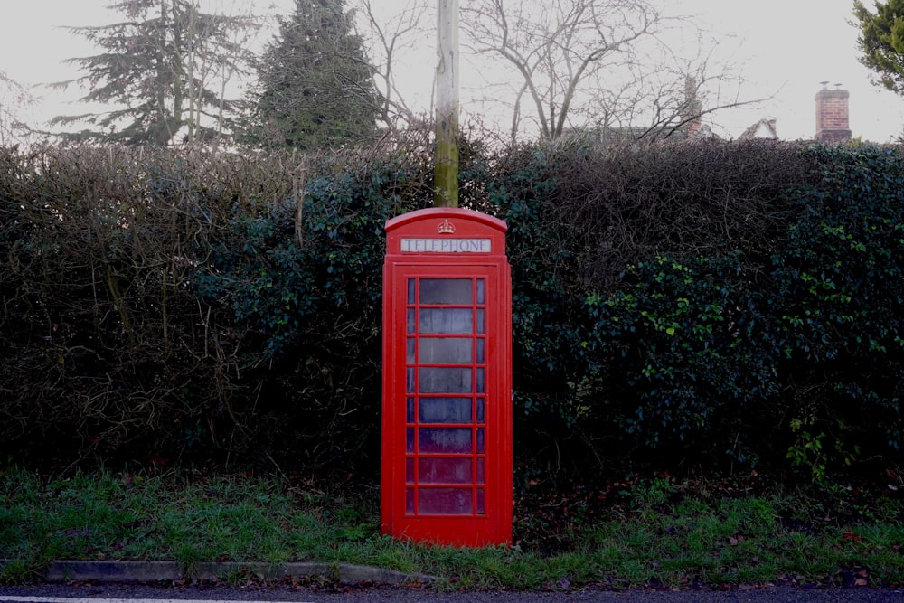 red telephone booth in front of green topiary