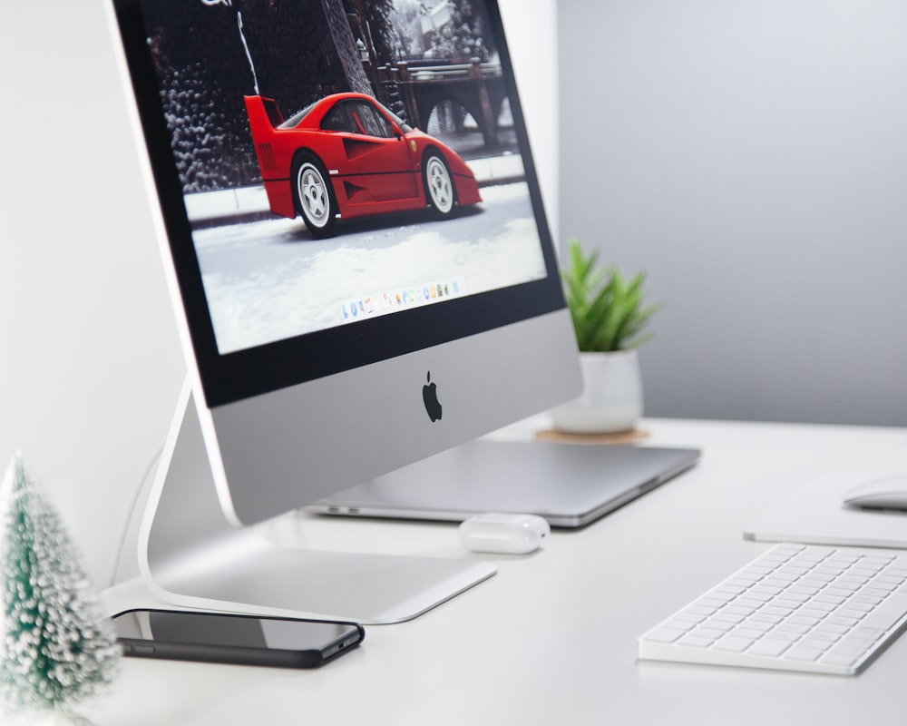 iMac plateado encendido que muestra un cupé rojo estacionado en el fondo de pantalla del pavimento