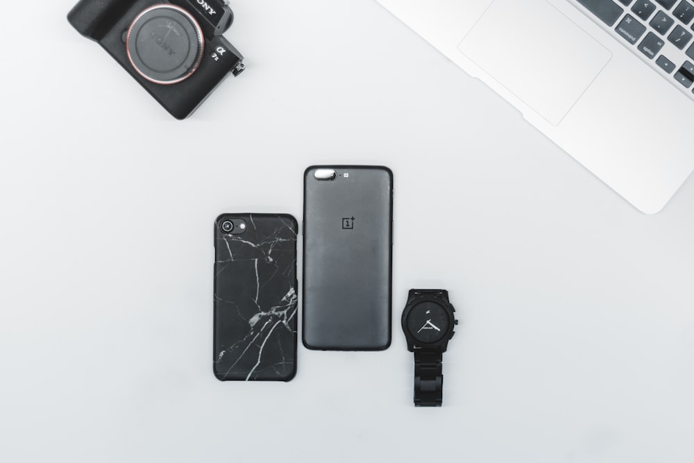 iPhone noir post-2017 à côté de la montre noire sur une surface blanche