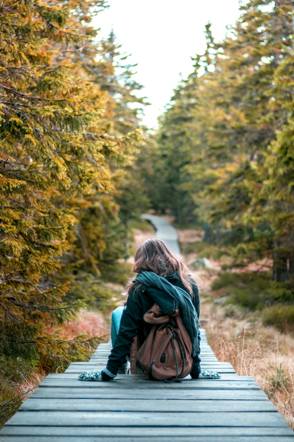 woman sitting on wooden pathway surrounded with trees