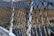 An intricately knotted rope netting attached to a white metal railing, with a blurred background of water and distant land. The netting features a series of diagonal crisscross patterns, showing wear and use.