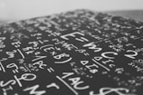 A close-up view of a chalkboard filled with various mathematical equations and symbols, written in white chalk on a dark surface. The focus is on the center, displaying formulas and expressions such as E=mc² among others.