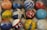 An array of colorful, vintage bowling balls with different markings and labels is arranged in a cardboard box. The balls display a variety of colors, patterns, and inscriptions, including names and numbers, adding a sense of history and personalization.