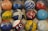 An array of colorful, vintage bowling balls with different markings and labels is arranged in a cardboard box. The balls display a variety of colors, patterns, and inscriptions, including names and numbers, adding a sense of history and personalization.