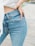 A person wearing light blue denim jeans with one hand resting on their hip. The jeans have a classic five-pocket design and appear to be high-waisted. Part of a white top and a wrist with a watch or bracelet are also visible.
