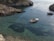 A small motorboat cruising near rocky cliffs under a bright blue sky in Calabria.