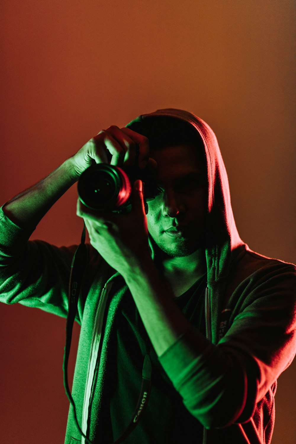 man in hooded jacket with camera by his face