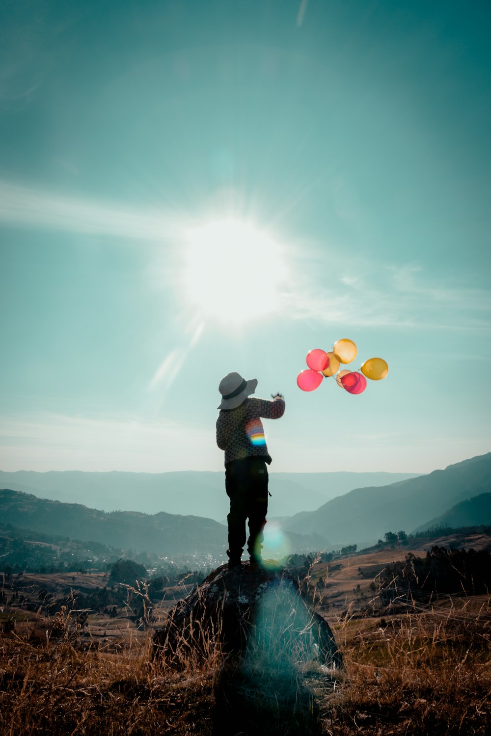 balloons flying near person standing on rock