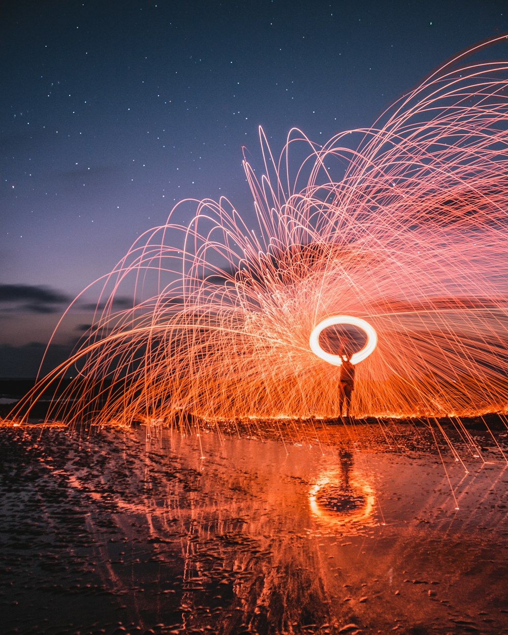 steel wool photography of man standing on body of water at nigh time