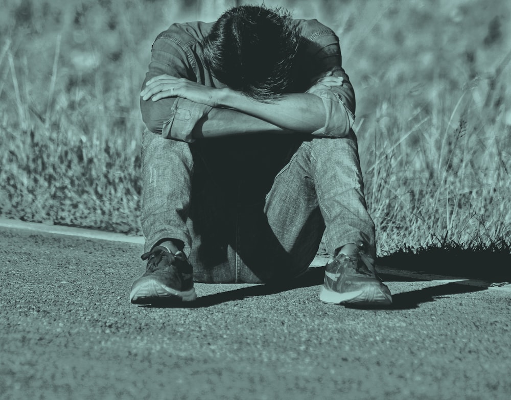 grayscale photo of man sitting on gray pavement road