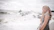 A young woman wearing a Kalima t-shirt standing on a volcanic beach with ocean waves in the background.