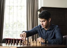 man in blue dress shirt sitting down and playing chess game