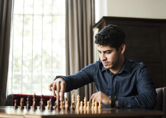 man in blue dress shirt sitting down and playing chess game