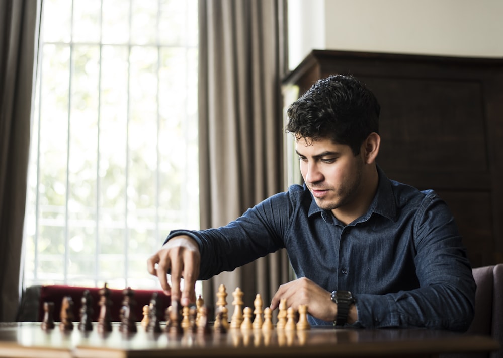 man in blue dress shirt sitting down and playing chess game