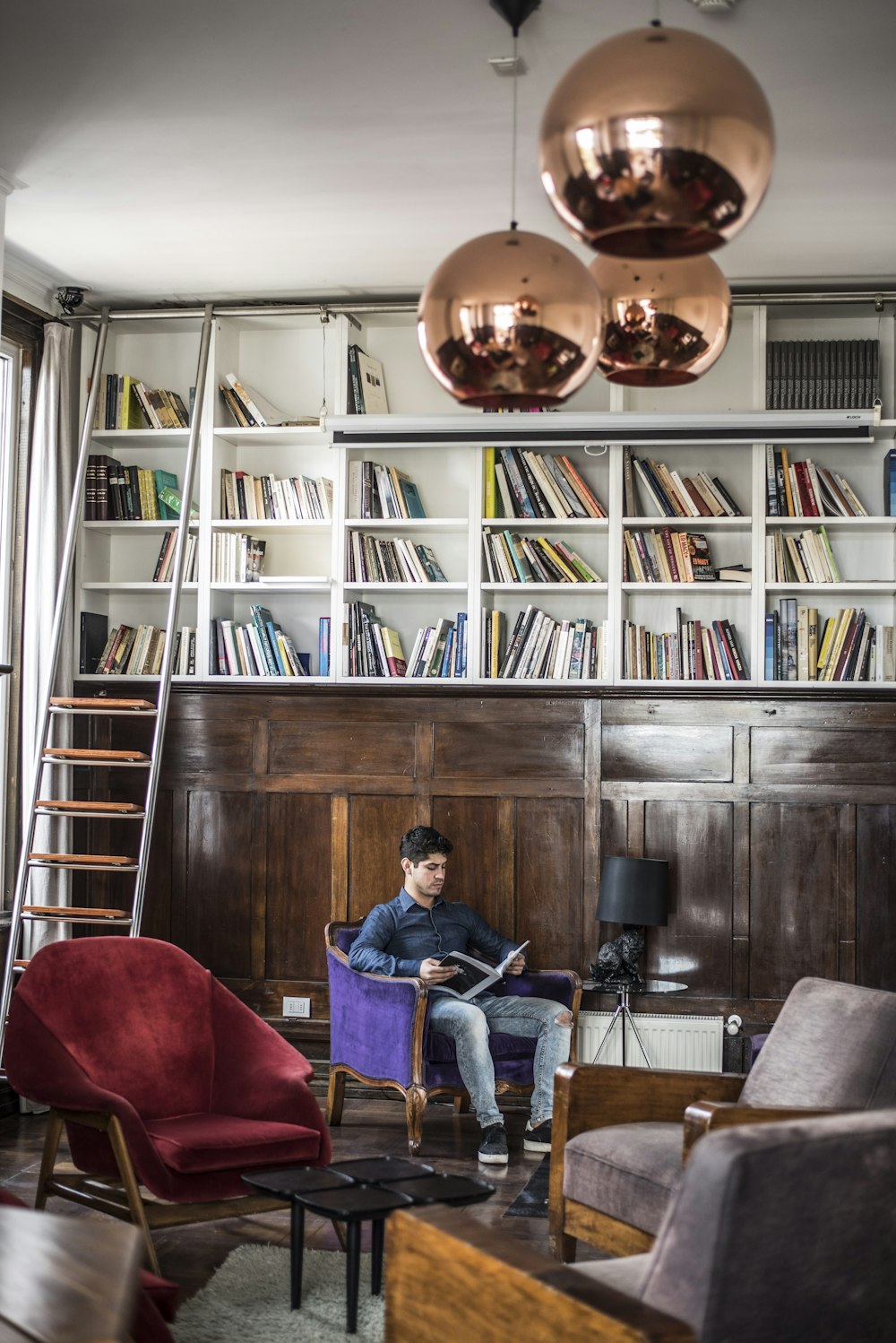 man sitting on purple chair beside bookshelves