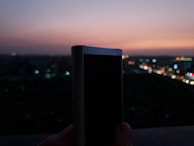 Close-up of a hand holding a compact Bluetooth device against a blurred cityscape.