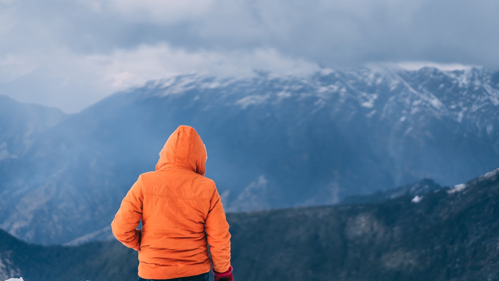 person wearing orange hoodie standing on mountain