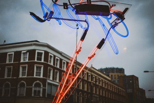 A vibrant blue and yellow pole sign glowing brightly against an evening sky on a busy city street.