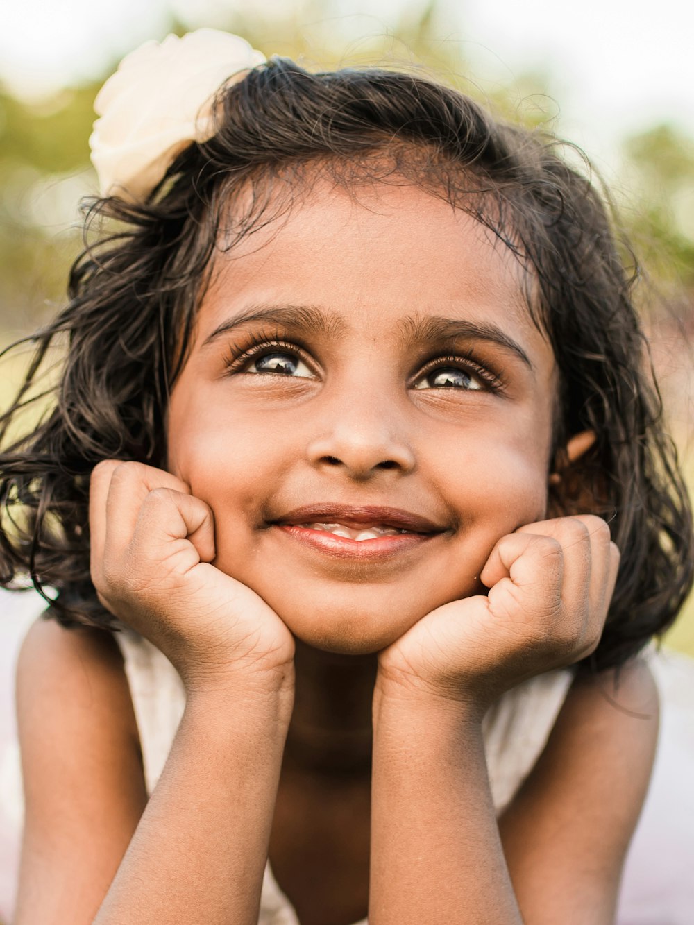 smiling girl wearing white tank top rest head on her two hands