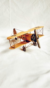 A model of a vintage biplane with wooden propellers and a yellow body is placed on a white surface. The plane features distinct cross insignias on the wings and has intricate detailing on its frame and wheels.