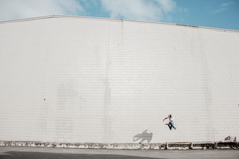 man jumping beside white concrete building