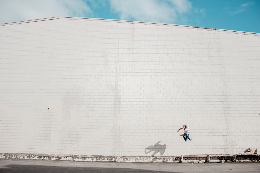 man jumping beside white concrete building