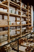 A bakery display with shelves filled with various containers and wooden boxes. The counter is lined with a variety of freshly baked goods, including muffins and pastries. The setting has a rustic and cozy atmosphere with wooden shelves and glass display cases.